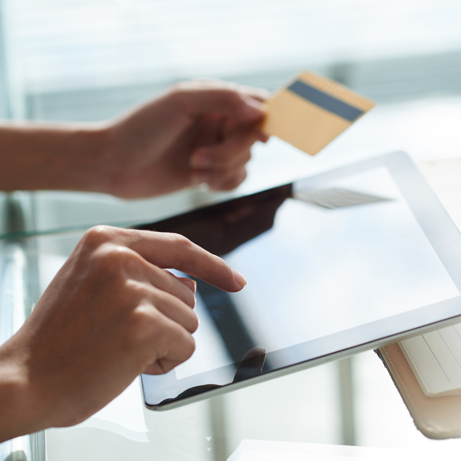 person holding credit card in the left hand and typing on an electronic tablet with the right hand